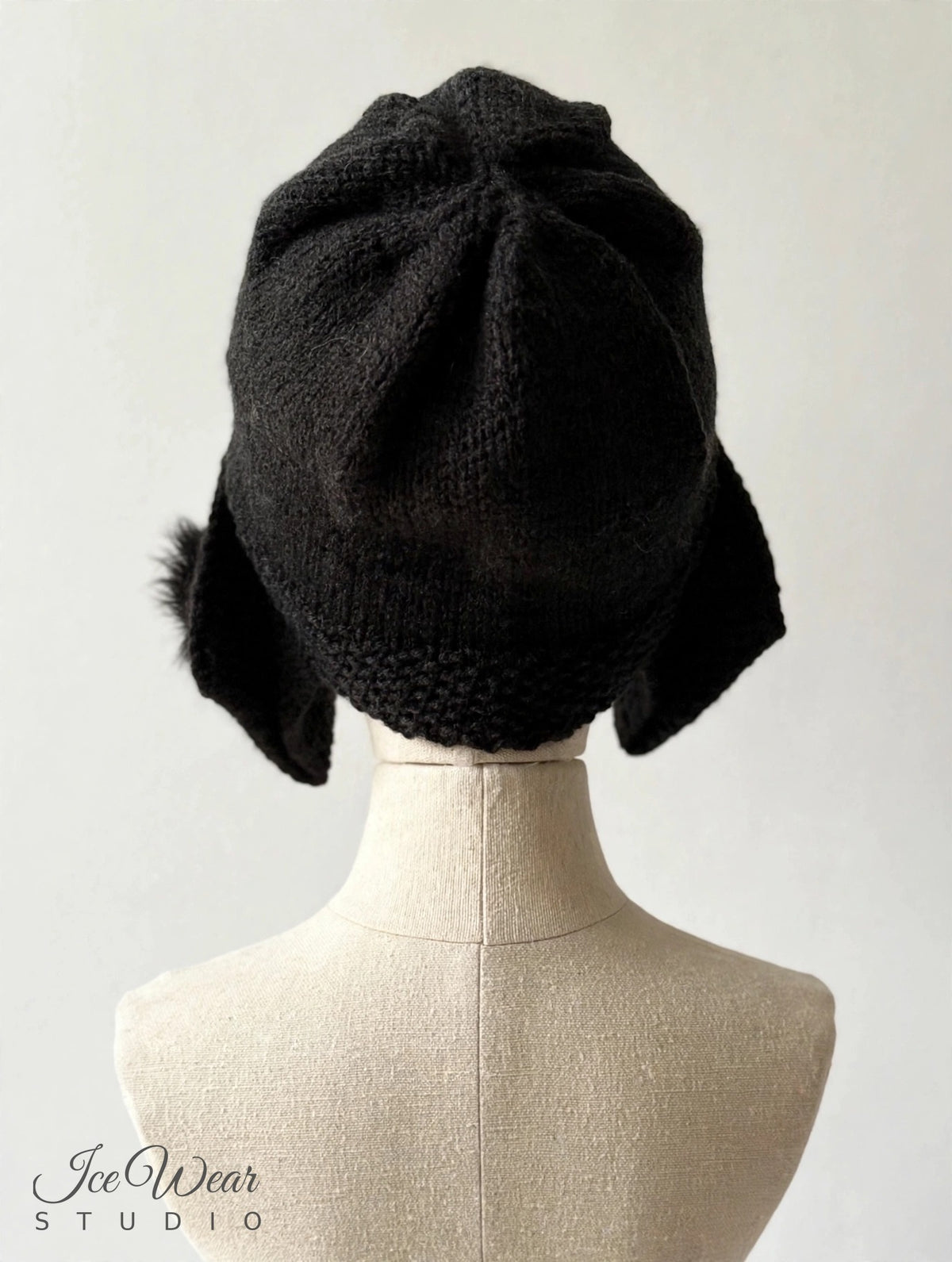 Black hand-knitted earflap cloche, back view showing gathered crown, on linen mannequin
